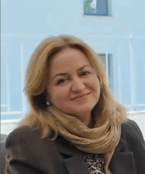 Усмихната жена с руса коса пред сграда